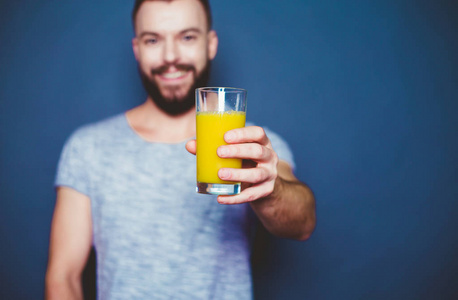 英俊的年轻人在一个灰色的背景下, 用一杯橙汁的新果汁 t恤衫。健康的生活方式