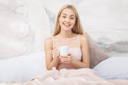 有吸引力的女人坐在她的床上喝茶