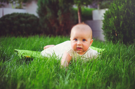 一个半岁的孩子在院子里的草地上爬行, 穿着一件白色的连衣裙, 6 月。儿童儿童用品的概念教育