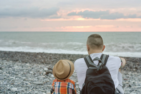 年轻的父亲和儿子坐在海滩海和夕阳的背景