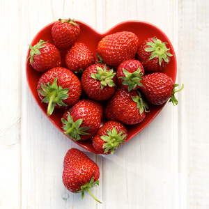 心形草莓和蓝莓在蓝色木背景美味的新鲜草莓在心形红碗和美丽的粉红色