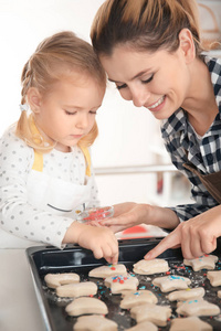 母亲和女儿装饰饼干面团在室内洒