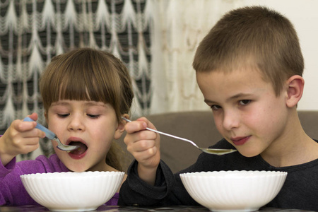 二个孩子男孩和女孩吃汤用匙子从盘子 wi
