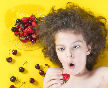 男孩兴奋地吃草莓。乌黑的头发，扎着马尾辫。草莓，樱桃成熟的红色