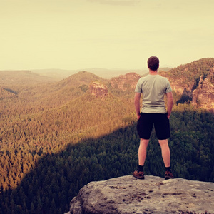 成人的灰色衬衫和黑裤子的徒步旅行者。高个子的砂岩悬崖看森林山谷到山顶
