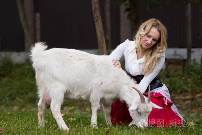 积极的女人抚摸山羊在绿色的林间空地