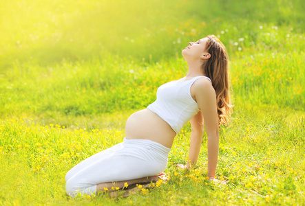孕妇做瑜伽的草地上行使和享有阳光明媚