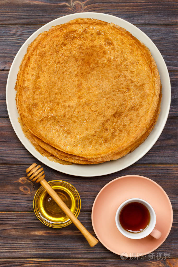 热的薄饼与蜂蜜和茶在盘子。茶和薄饼早餐