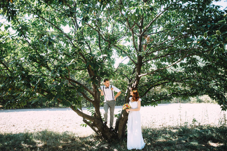新郎与他美丽的红头发的新娘站在一棵高大的绿树