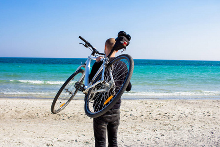 男性与自行车, 年轻人在黑色休闲穿戴, 骑自行车的人在海滩在晴朗的天