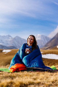 愉快的女孩坐在睡袋在高加索山的背景