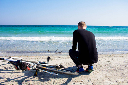 男性与自行车, 年轻人在黑色休闲穿戴, 骑自行车的人在海滩在晴朗的天