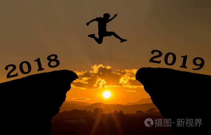 一个年轻人跳跃在2018和2019年之间在太阳和通过在小山剪影晚上五颜六色的天空的空白。新年快乐2018