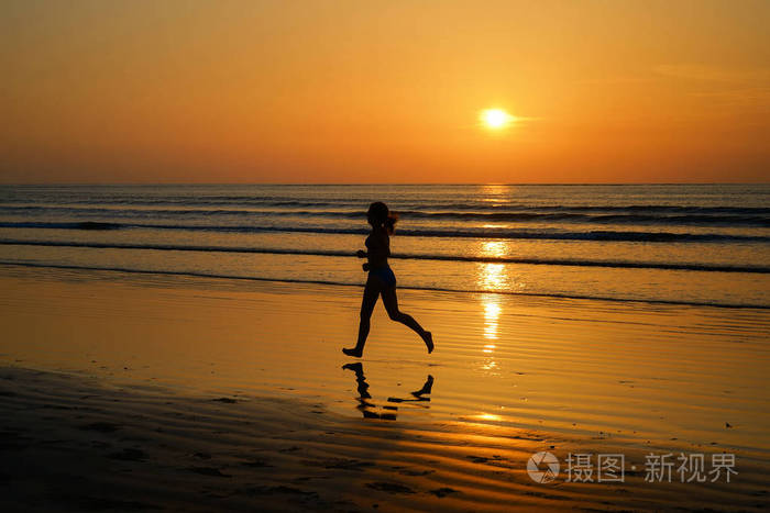 女人慢跑者在反思健身与体育概念的日落海滩上运行的剪影