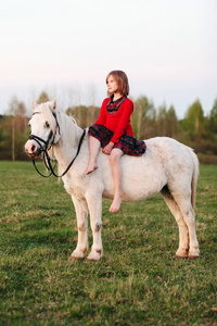 坐在一匹白马上穿裙子的小女孩遥望远方
