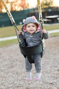 非常快乐的小女孩在一个秋千上的鼠标动物服装。微笑一岁的孩子