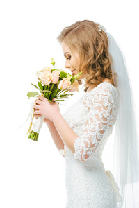 有吸引力的新娘在婚纱礼服和面纱的侧面, 在白色的鲜花隔离的花束