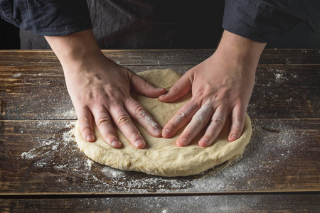 在木制背景下准备面团的男厨师手特写照片