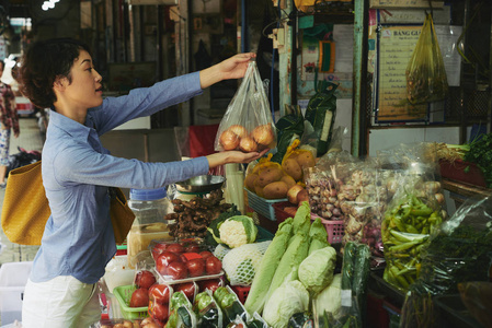 女人在食品市场买了一大包成熟的洋葱