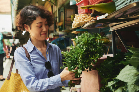 亚洲年轻女子在食品市场买一束绿色植物