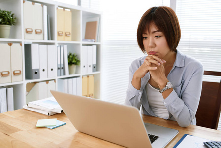 忧郁的日本女性商务主管在笔记本电脑屏幕上阅读信息