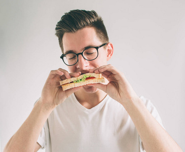男人拿着一块汉堡包。学生吃快餐。不是有用的食物。非常饥饿的人。书戴着眼镜