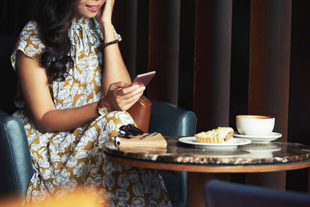 在咖啡馆里喝咖啡和甜点时, 女人发短信给朋友的画面照片