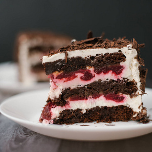 与樱桃和酸奶馅的巧克力蛋糕的密切的看法在黑木桌背景在白色板材与餐巾服务