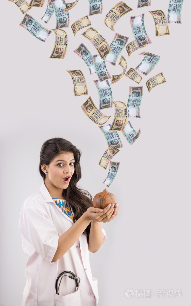 印度女医生抱着存钱罐或钱框组成的粘土和印度货币从天空, 印度货币雨