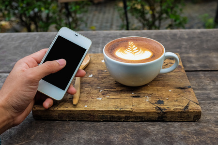智能手机与杯拿铁艺术牛奶咖啡离开纹理上木制背景，Clos 了业务对象