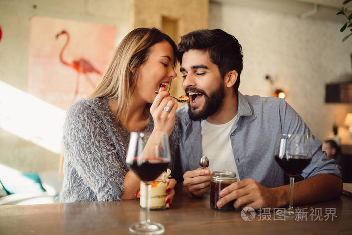 女孩喂养她的男朋友与蛋糕在咖啡馆, 喝葡萄酒和庆祝情人节