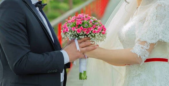 他们手里捧着粉红色的花花束。双手合拢在背后, 捧着一束美丽的玫瑰花束。新婚夫妇在他们手中举行婚礼花束在每个 o 之间