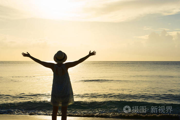 女人的剪影双臂张开面对日落的海滩