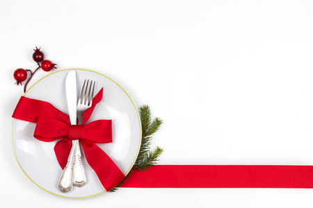 圣诞餐桌上设置有盘子, 餐具, 松树枝, 缎带和红色浆果。冬季假期和节日背景。圣诞前夕晚餐, 新年食品午餐