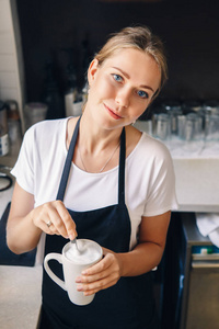 年轻美丽的白种女人的肖像咖啡搅拌泡沫在杯卡布奇诺。人在工作, 小企业概念