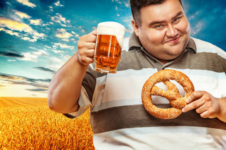 年轻的胖男人在慕尼黑啤酒节，喝啤酒和吃椒盐脆饼在黄色背景上