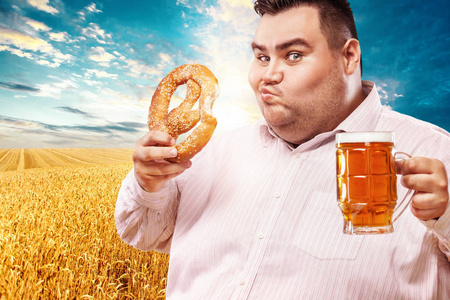 年轻的胖男人在慕尼黑啤酒节，喝啤酒和吃椒盐脆饼在黄色背景上