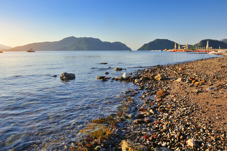 早上海景与卵石的海滩和山区的背景