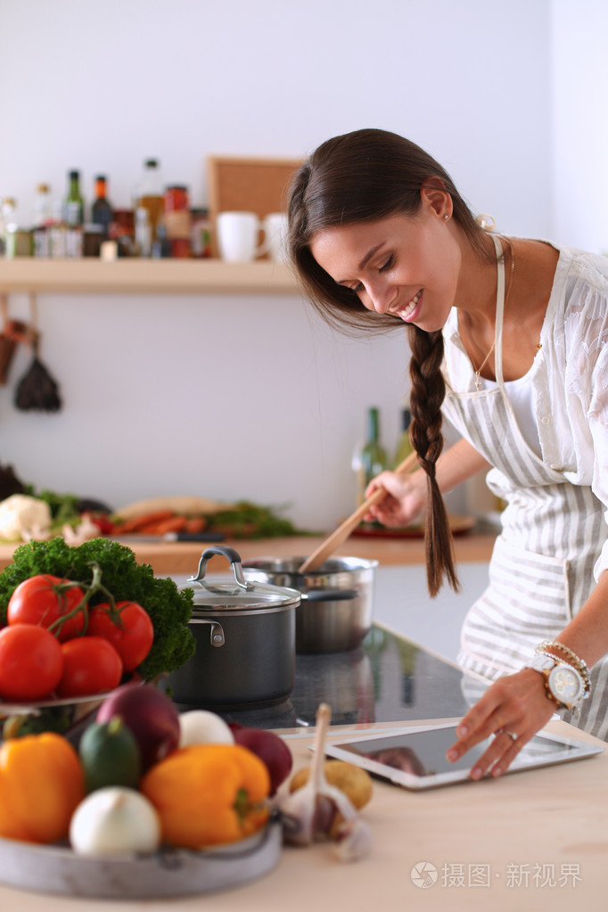 使用一台平板电脑,在她的厨房里做饭的年轻女人