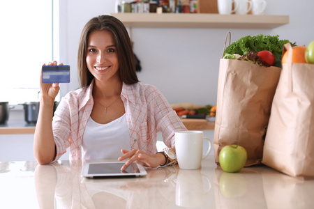 面带笑容的女人，网上购物在厨房中使用平板电脑和信用卡