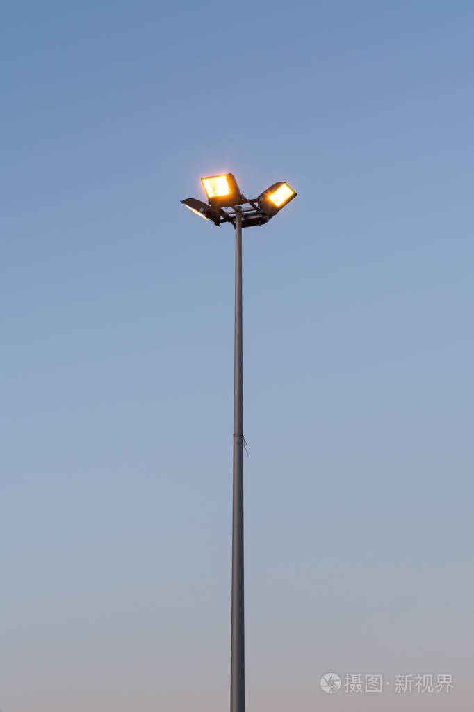 路灯与四泛光灯闪耀着黄色的光芒在傍晚对一个蓝色的黑暗的天空透视