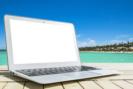 在木桌上的笔记本电脑。顶级海景。热带海岛背景。打开空白笔记本电脑空空间。带复制空间的前视图。隔离的白屏