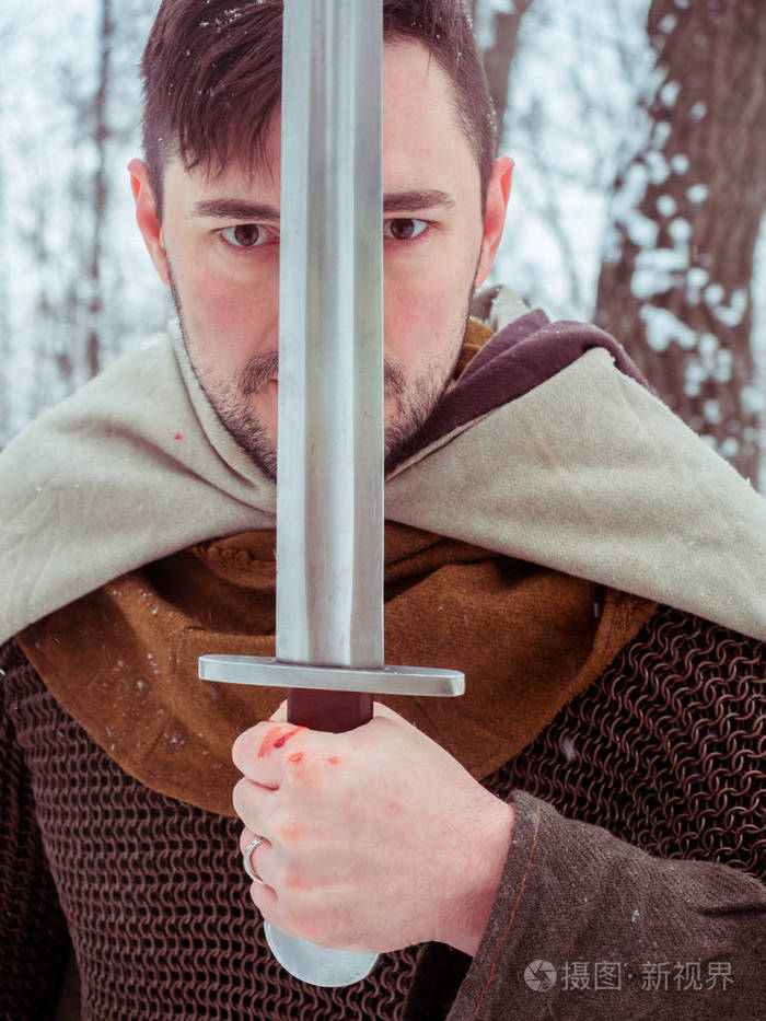 中世纪维京勇士在链邮件和头盔持有剑在冬季森林