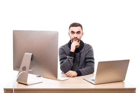 自信的生意人坐在桌上与膝上型电脑和个人计算机和看照相机隔绝在白色背景