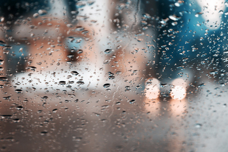 滴的雨水蓝色玻璃背景。街头的散景灯熄灭