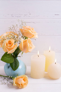 燃烧的蜡烛和玫瑰花白色木制背景上的蓝色花瓶里。选择性的焦点