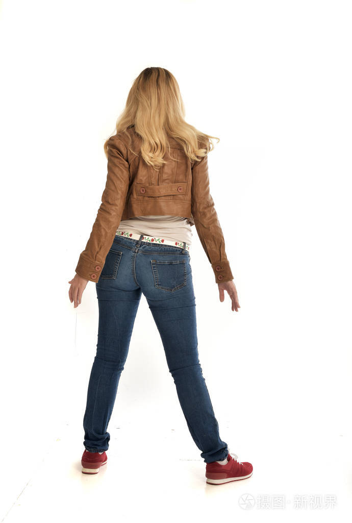 穿着棕色夹克和牛仔裤的金发女郎的全长肖像.在白色背景上站立姿势