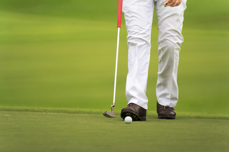 高尔夫球手走在绿色的推杆