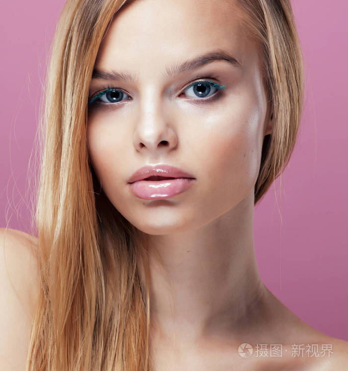 年轻漂亮金发女人的发型靠拢和化妆上粉红色背景微笑