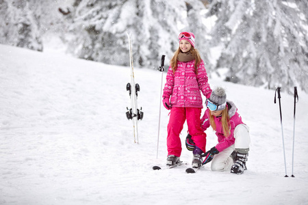 母亲帮助她的女儿正确地把滑雪鞋放在滑雪板上